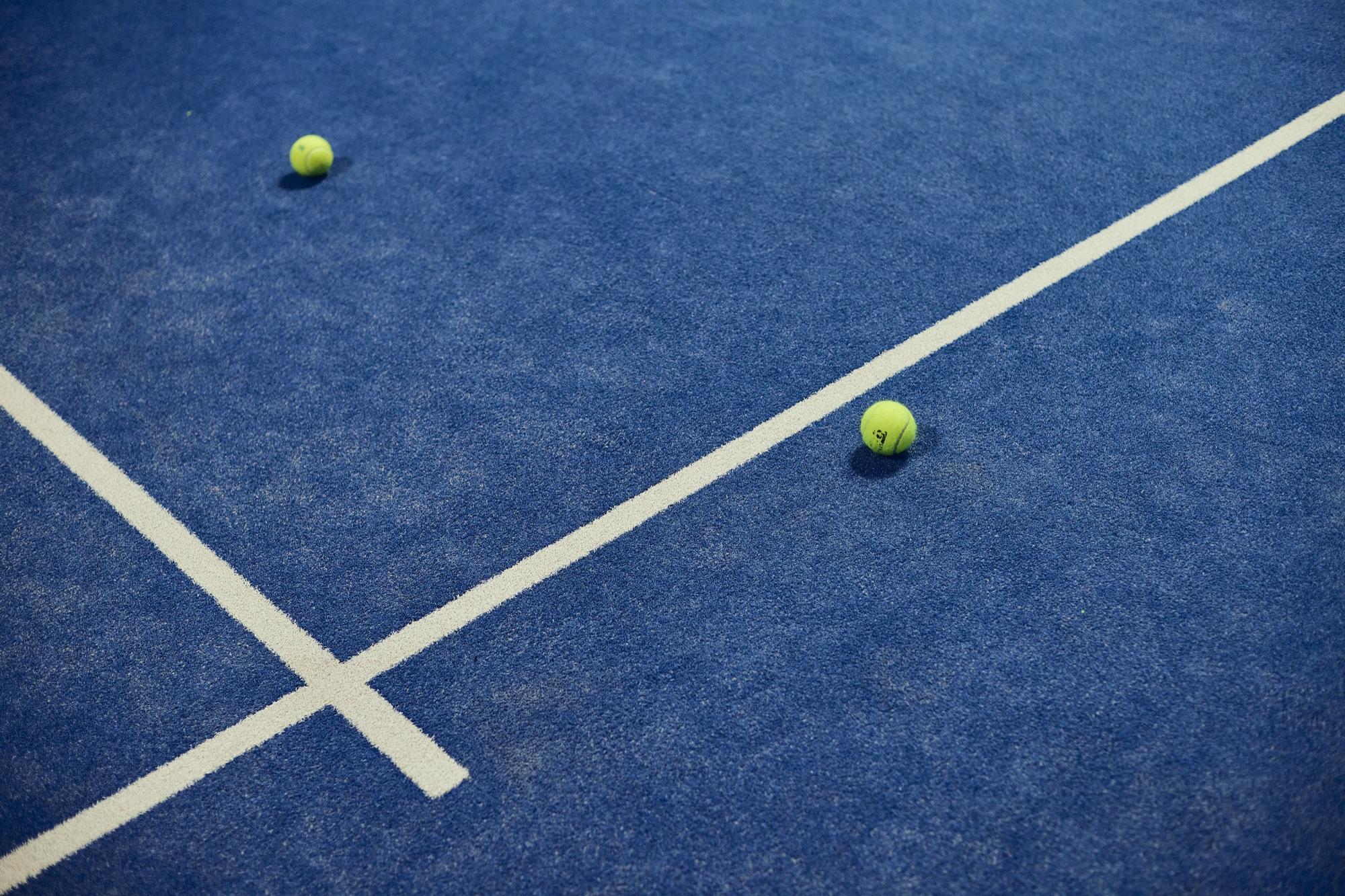 Blue indoor padel court with two balls on the line